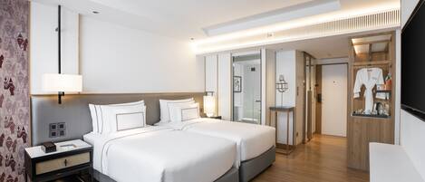 A modern hotel room with two beds, a bedside table, a lamp, a wardrobe, and a mirror.
