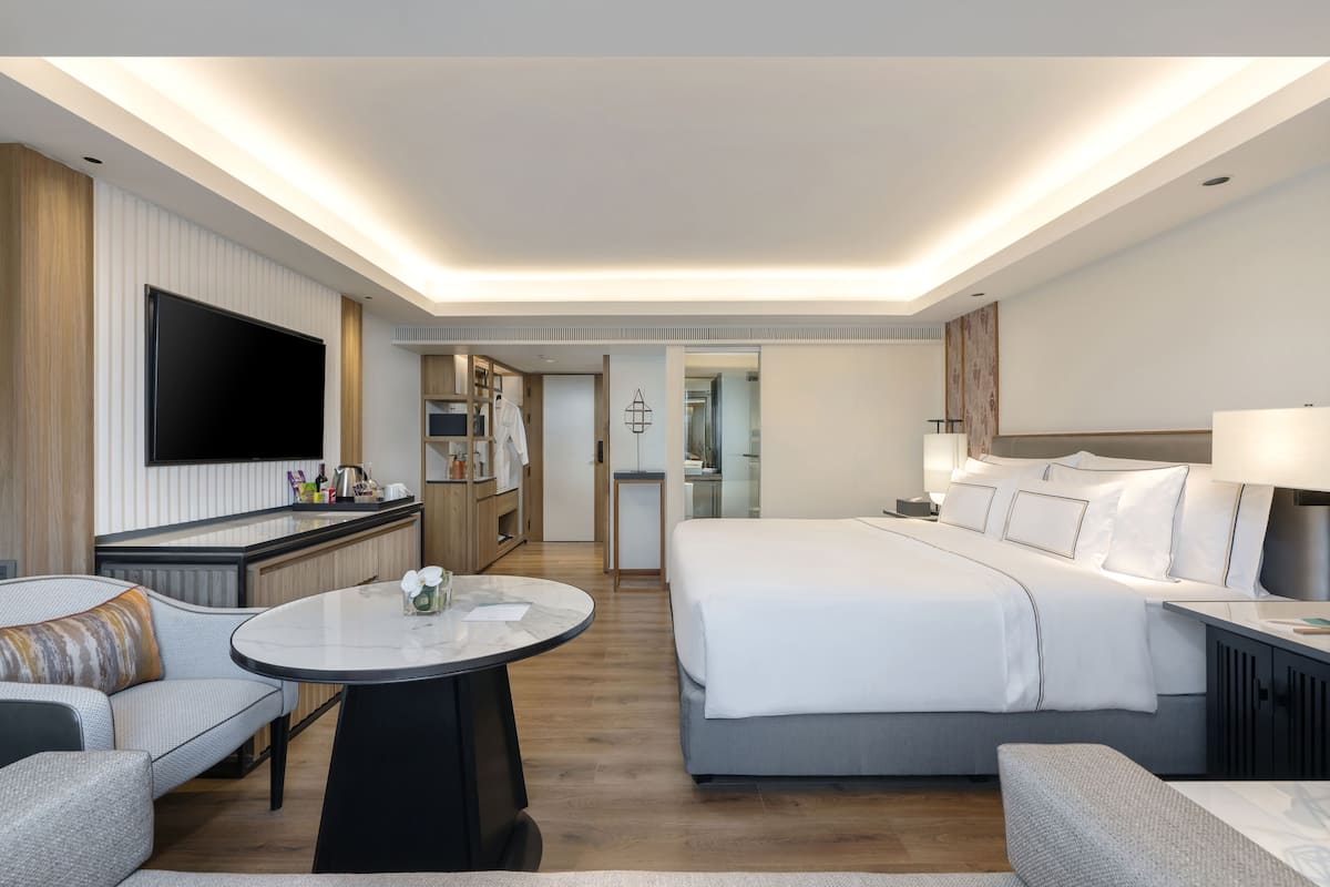 Ein modernes Hotelzimmer mit einem großen Bett, einer Couch, einem Esstisch, einem Fernseher und einer Küchenzeile.