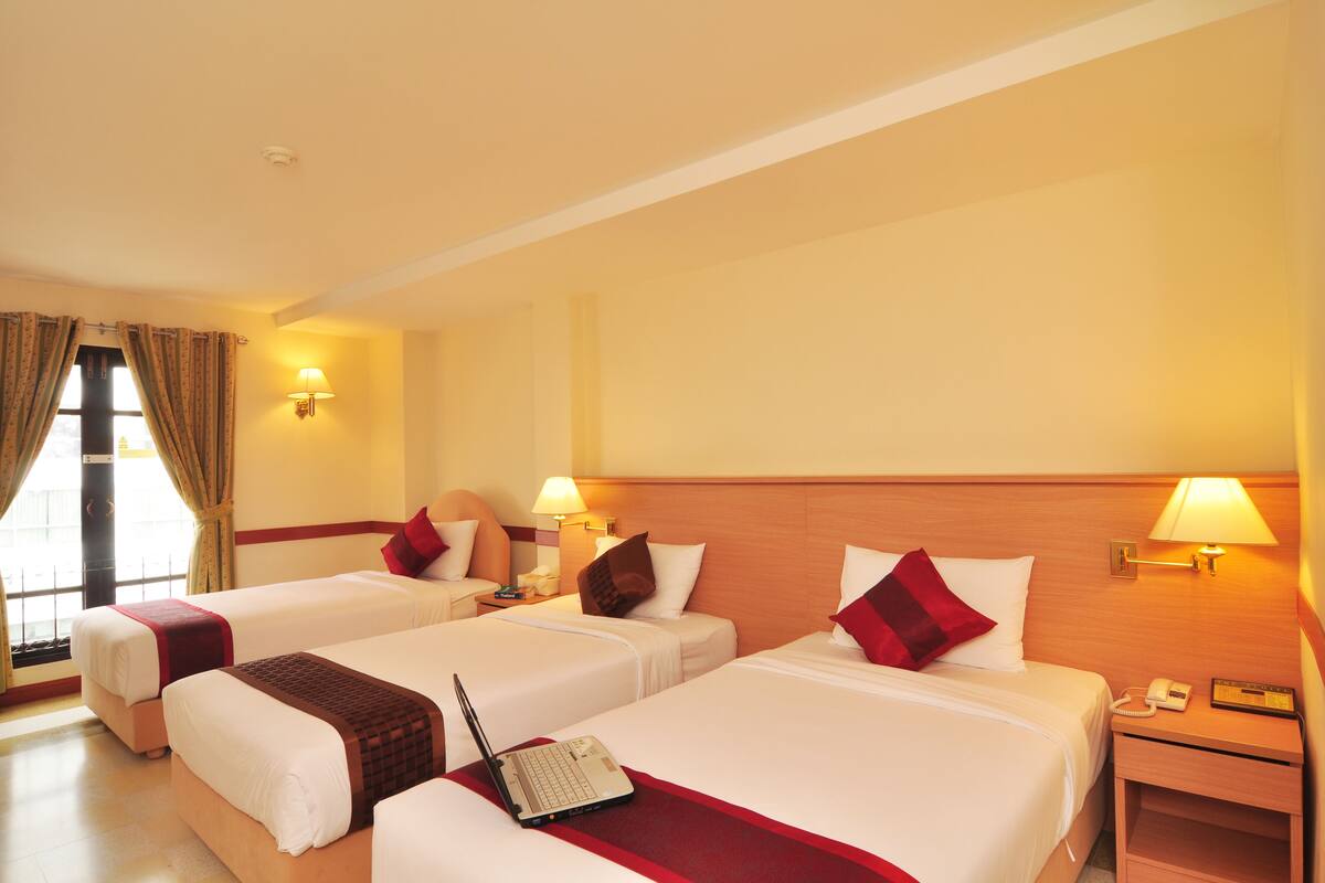 A hotel room with two beds, a desk, a lamp, and a window with curtains.