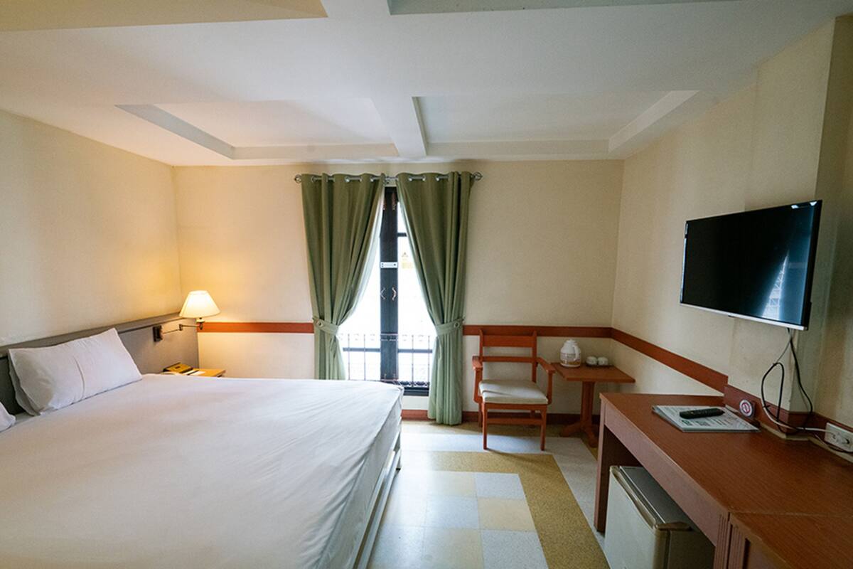 A hotel room with a bed, a desk, a chair, a television, and a window with curtains.