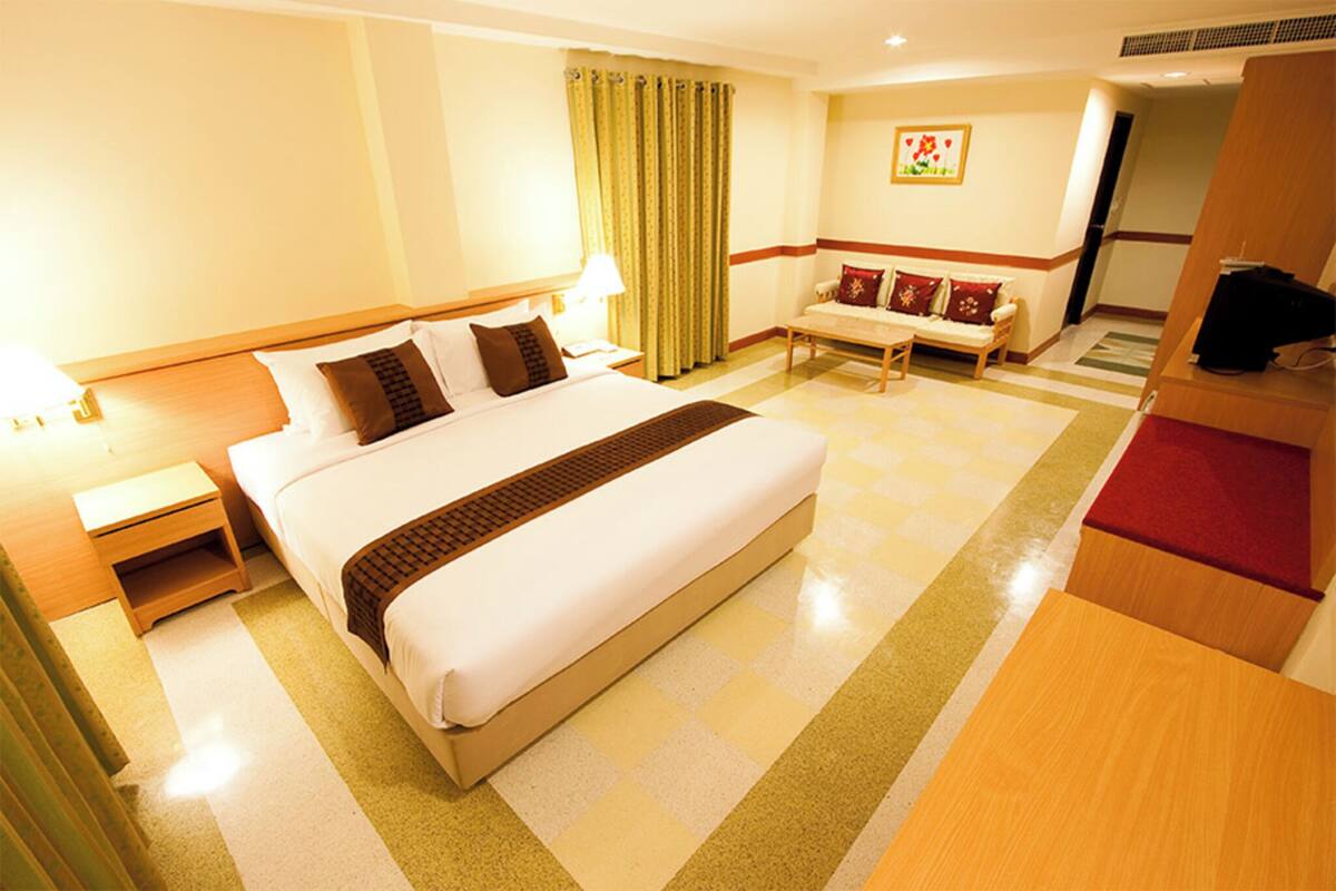 A hotel room with a large bed, a bedside table, a desk, a chair, a sofa, and a television.
