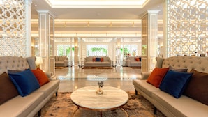 A spacious lobby with a high ceiling, two sofas with cushions, a marble coffee table, and decorative screens.