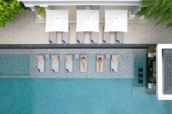 An aerial view of a swimming pool area with lounge chairs and umbrellas, a tiled walkway, and a small indoor area with a sink and a plant. - The Beverly Hotel Pattaya (Pattaya)