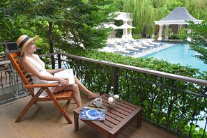 A woman sitting on a wooden chair overlooking a pool with lounge chairs and umbrellas. - The Beverly Hotel Pattaya (Pattaya)