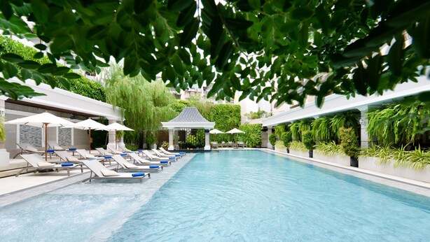 A swimming pool with lounge chairs and umbrellas, surrounded by greenery and a gazebo.