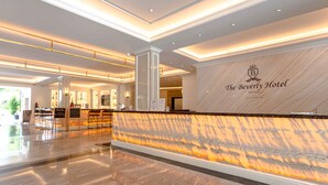 A spacious lobby with a marble reception desk, a sign for The Beverly Hotel Pattaya, and a clean, modern design.