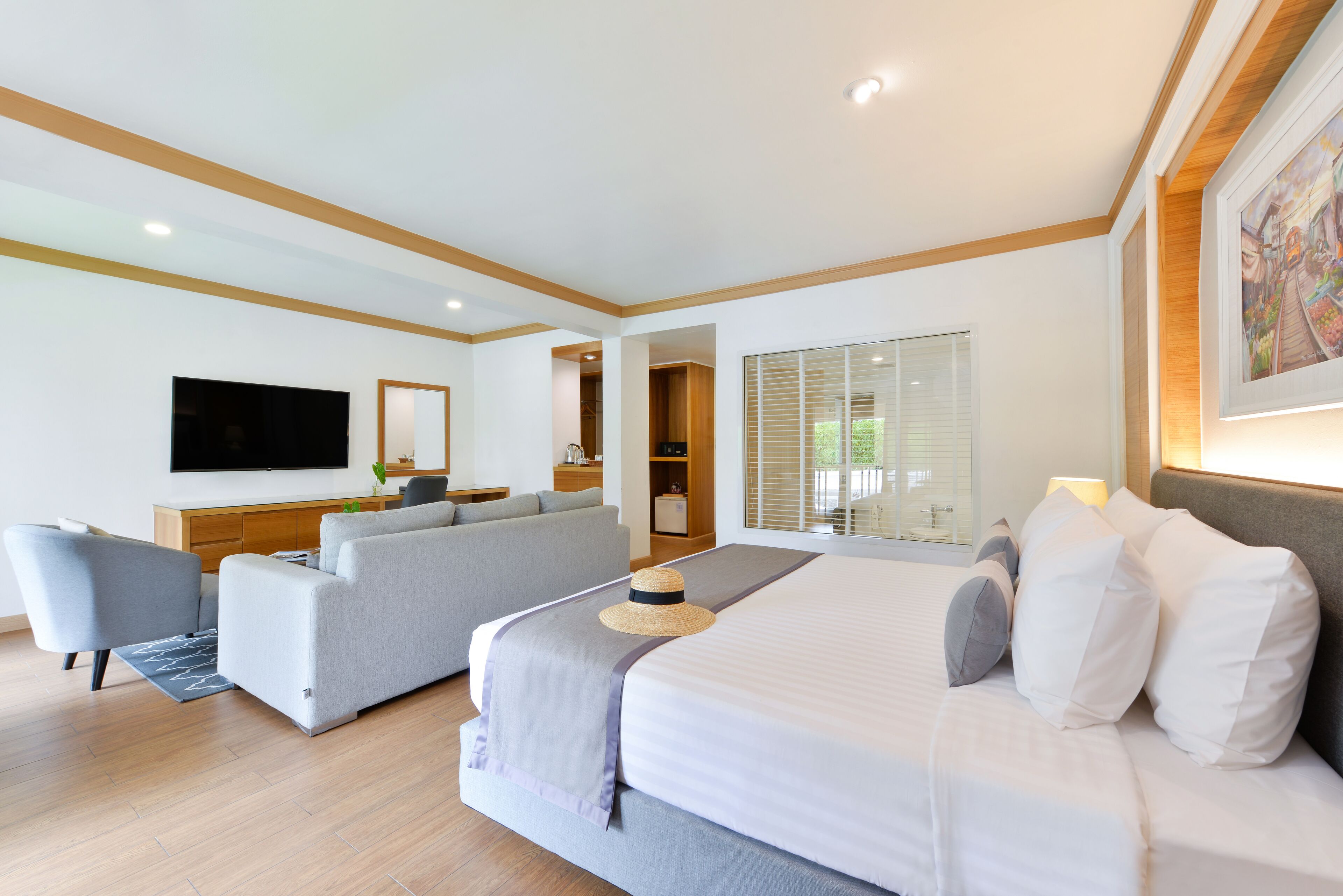 A modern hotel room with a large bed, a sofa, a TV, and a dining area.