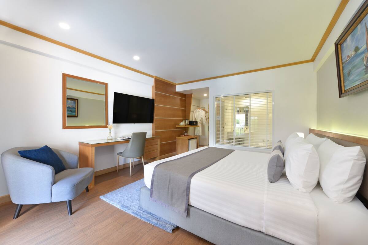 A modern hotel room with a large bed, a desk, a chair, and a TV.