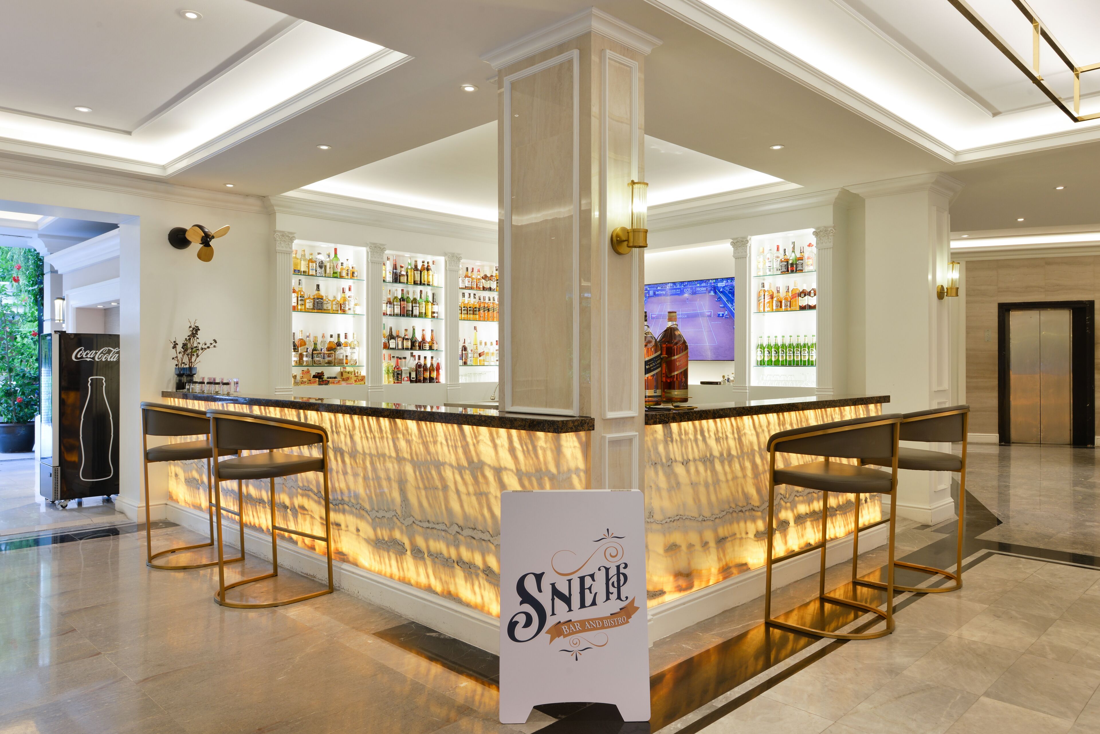 A bar area with a marble countertop, bar stools, and shelves of liquor bottles.