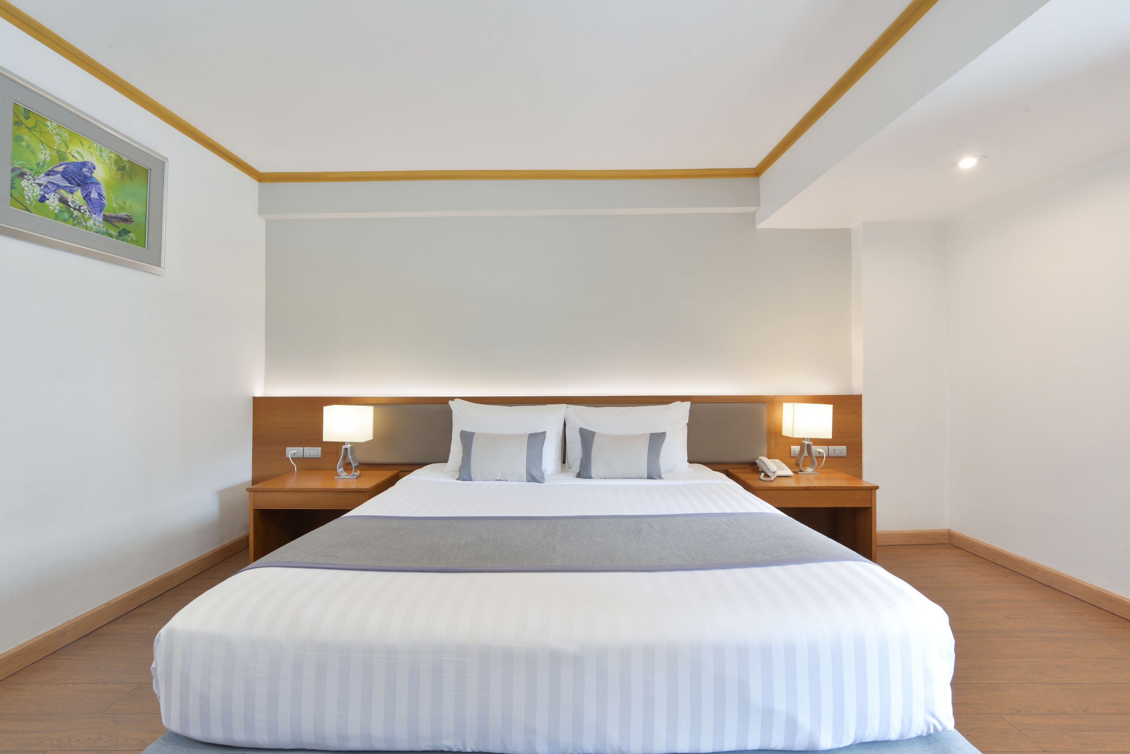 A hotel room with a large bed, two bedside tables with lamps, a wooden headboard, and a framed picture on the wall.