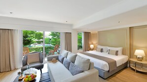 A hotel room with a large bed, a sofa, a dining table with fruit, and a view of the outdoors.