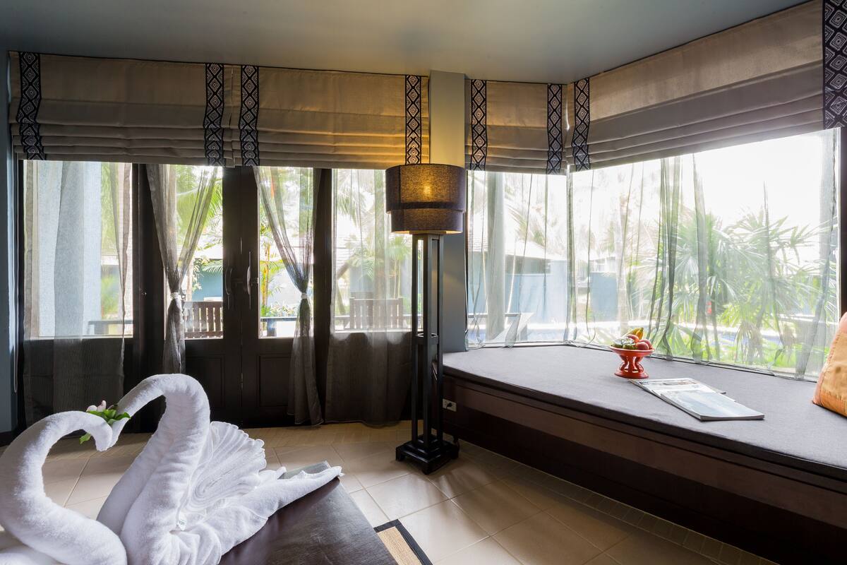 Una habitación con una cama, un ventanal con cortinas, una lámpara de pie y un adorno con forma de cisne.