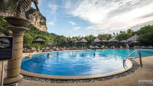 A swimming pool with lounge chairs and umbrellas, surrounded by palm trees and a mountain backdrop. - Peace Laguna Resort & Spa (Krabi)