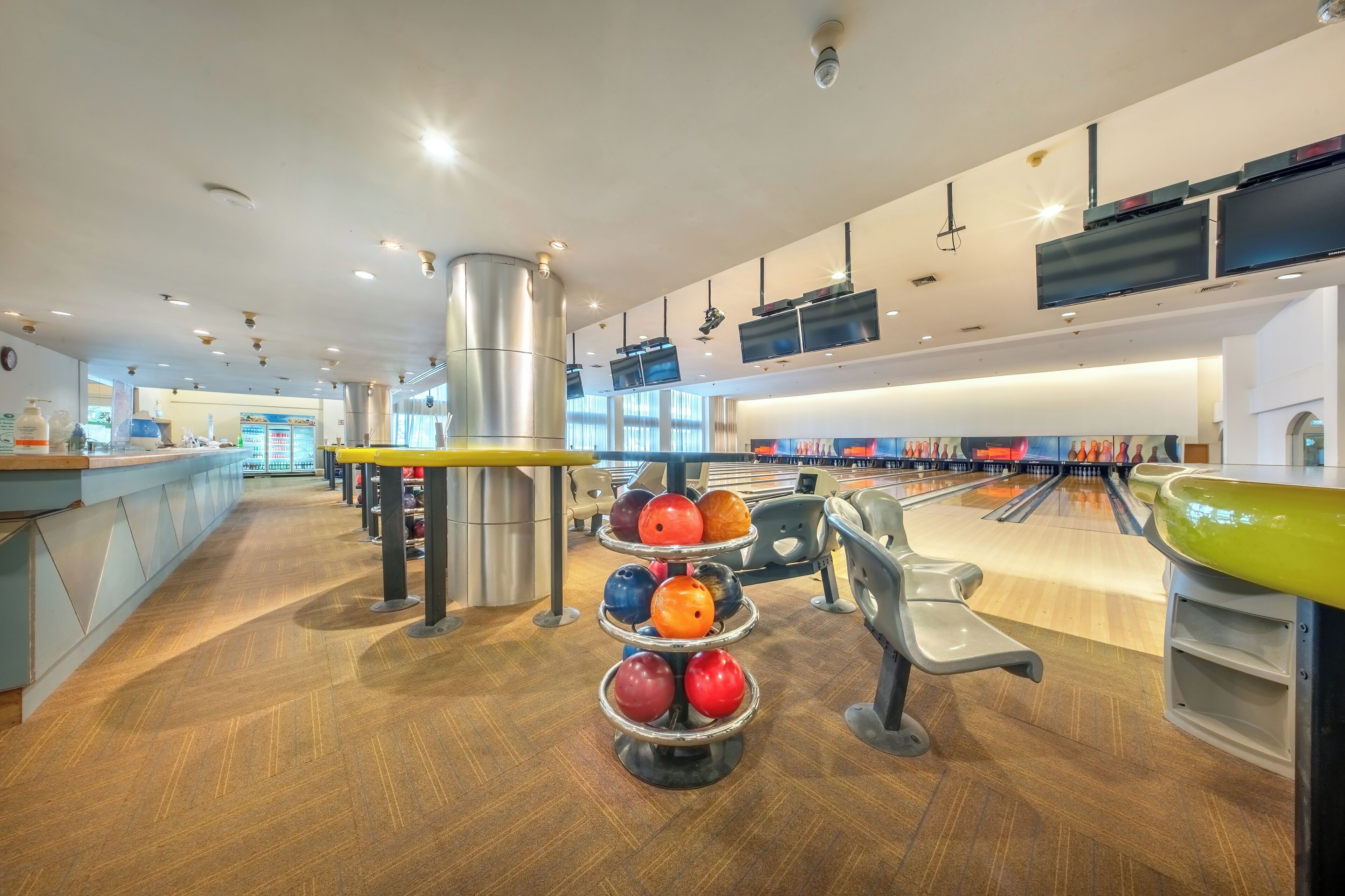 A bowling alley with multiple lanes, a bowling ball rack, and seating areas.