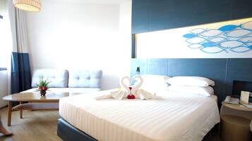 A hotel room with a large bed, a bedside table, a small table with a vase, a sofa, and a wall art piece.