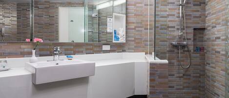 A modern bathroom with a white sink, a glass shower enclosure, and a mirror with a brick-patterned wall.