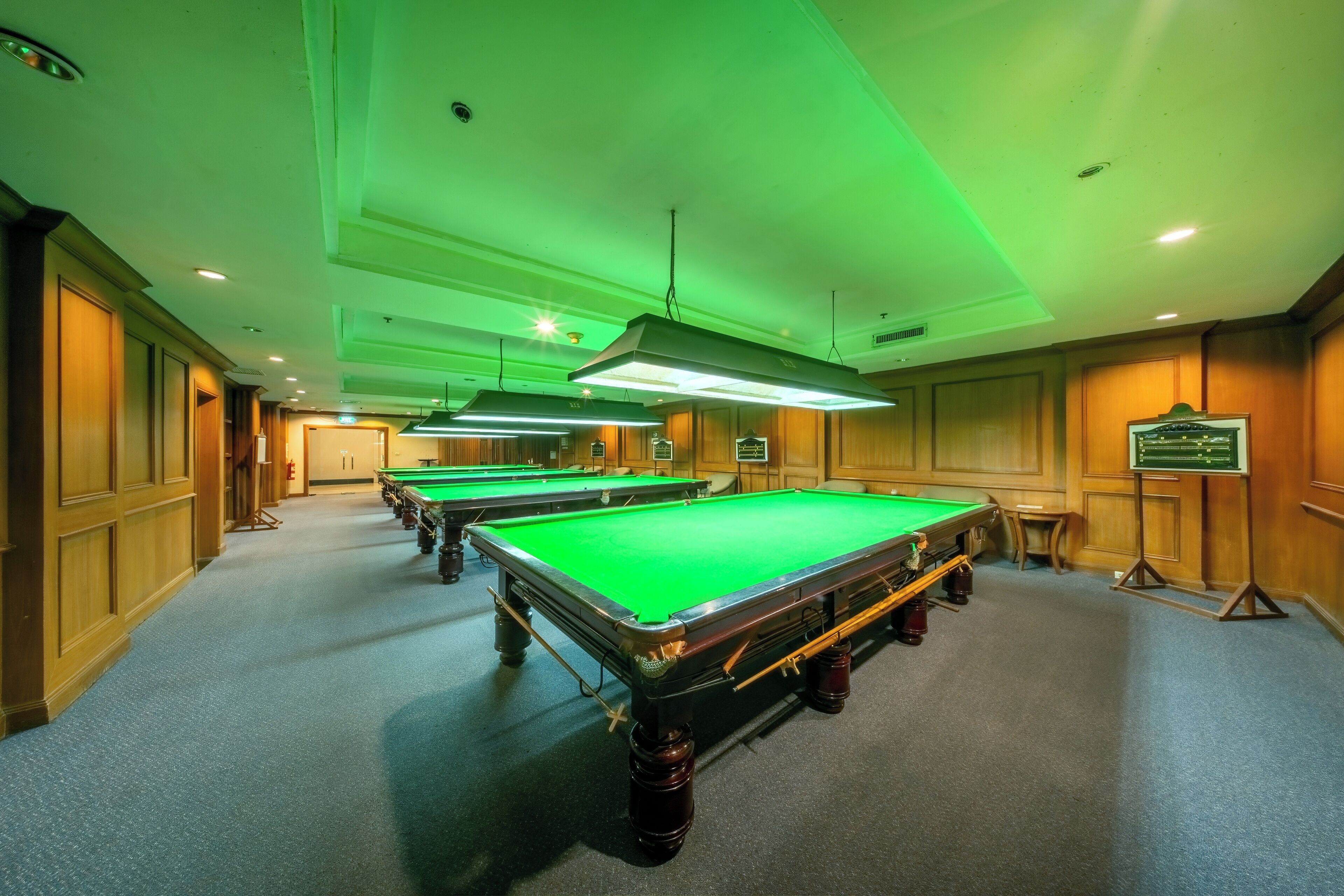 Una sala de billar con varias mesas y superficie de fieltro verde.