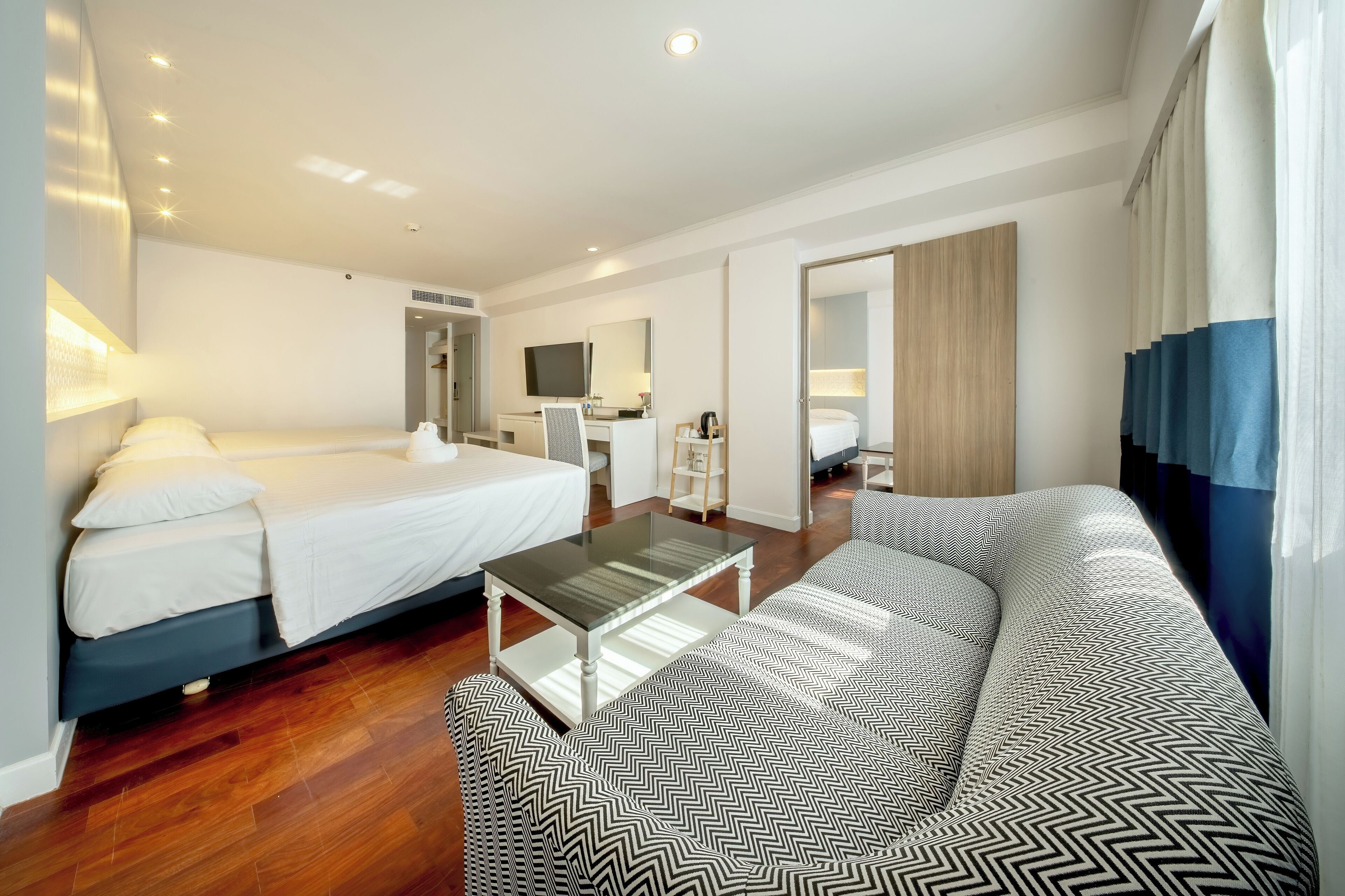 A hotel room with a bed, a sofa, a coffee table, a desk, and a TV.