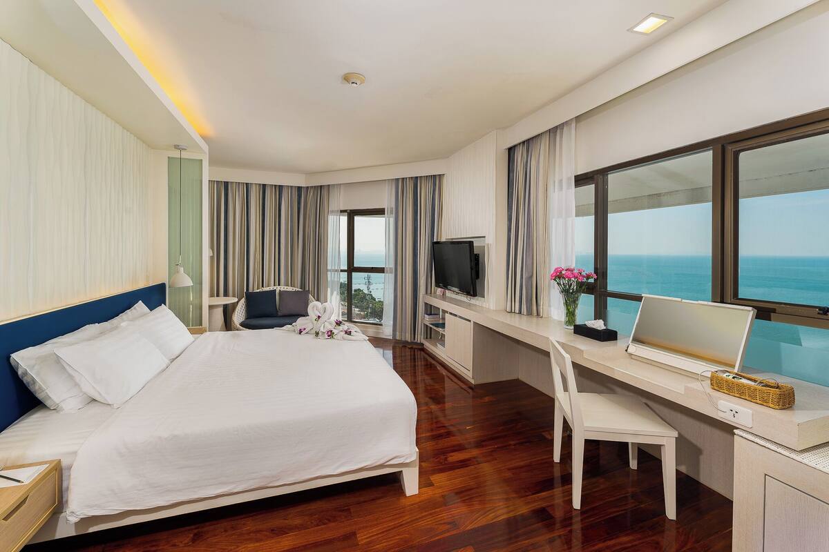 A hotel room with a large bed, a desk with a laptop, a TV, and a view of the ocean.