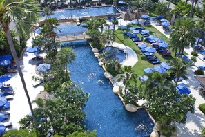 Un área de piscina en un complejo turístico con varias piscinas, sillas de descanso y sombrillas.