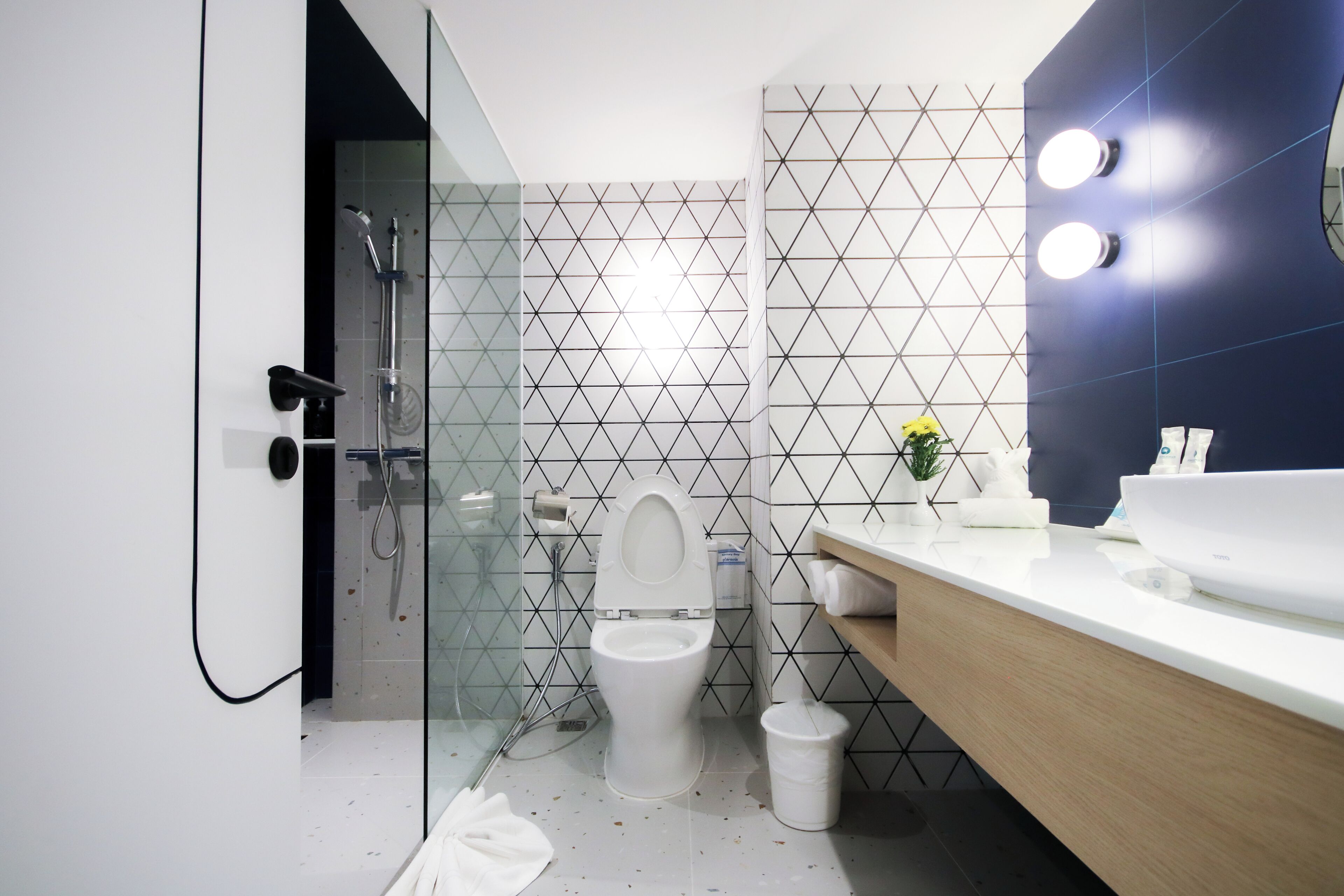 Une salle de bain moderne avec une douche à parois de verre, des toilettes blanches et un meuble-lavabo en bois avec un lavabo blanc.