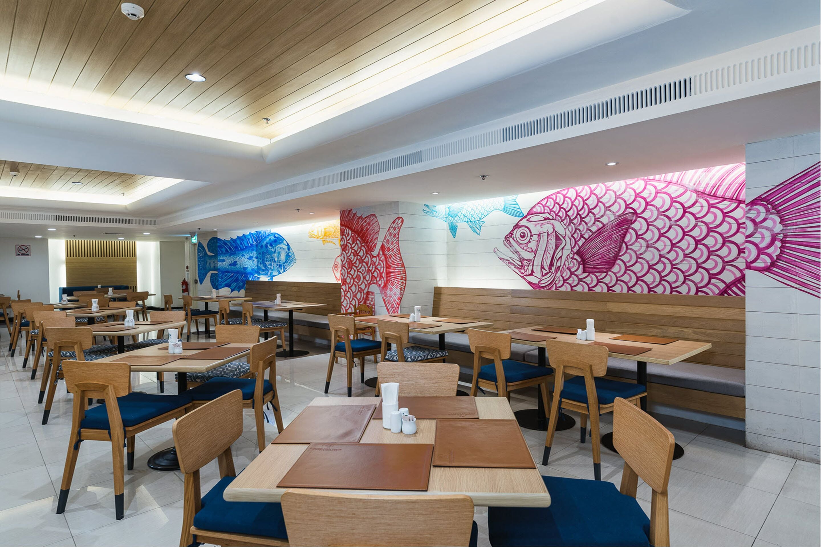 A restaurant with wooden tables and chairs, a high ceiling, and a wall mural of fish.