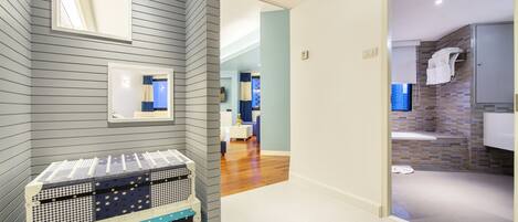 A hotel room with a grey striped wall, a check-in counter, a bathroom with a shower and a sink, and a hallway leading to another room.