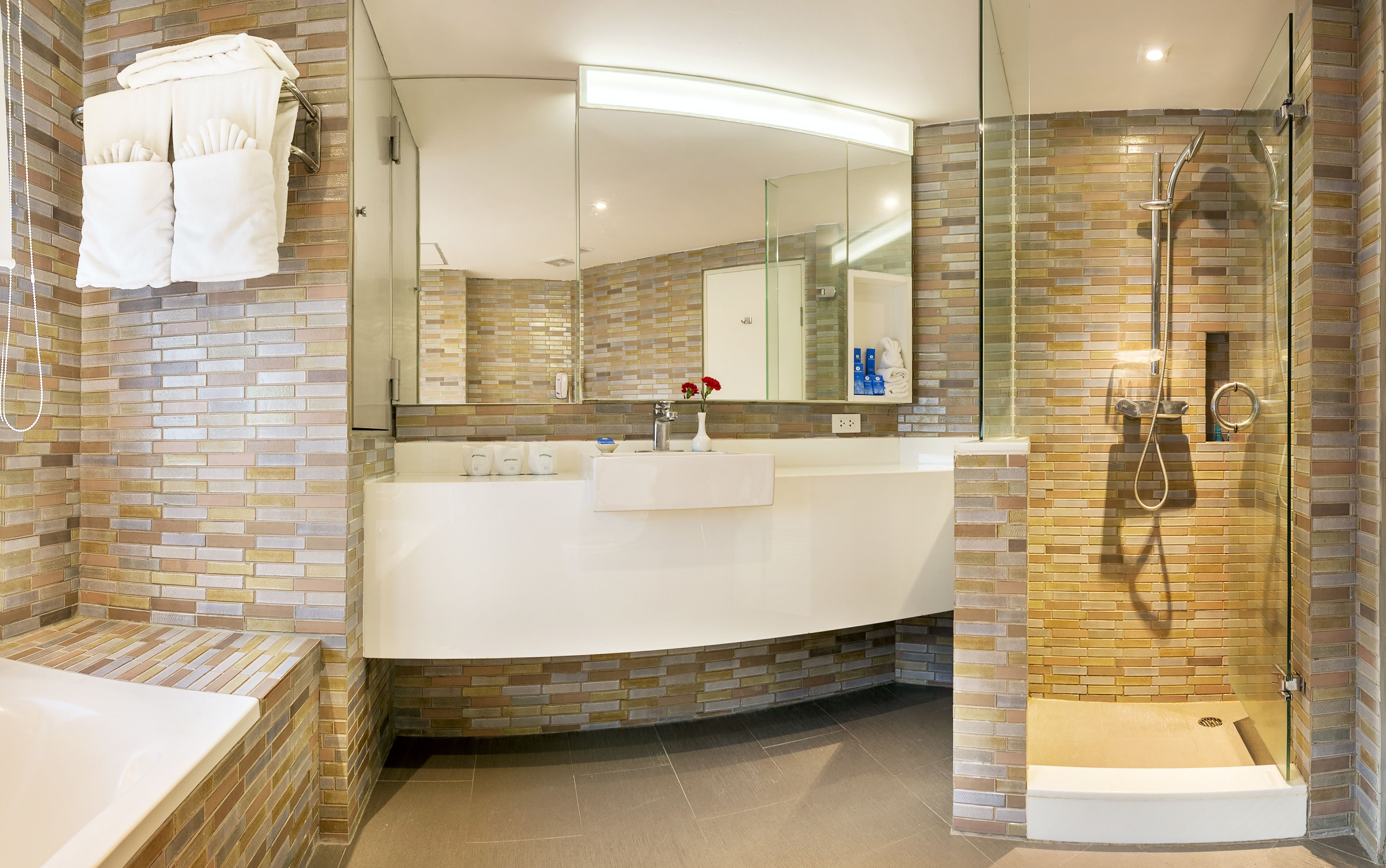 A modern bathroom with a curved vanity, a glass shower enclosure, and a brick accent wall.