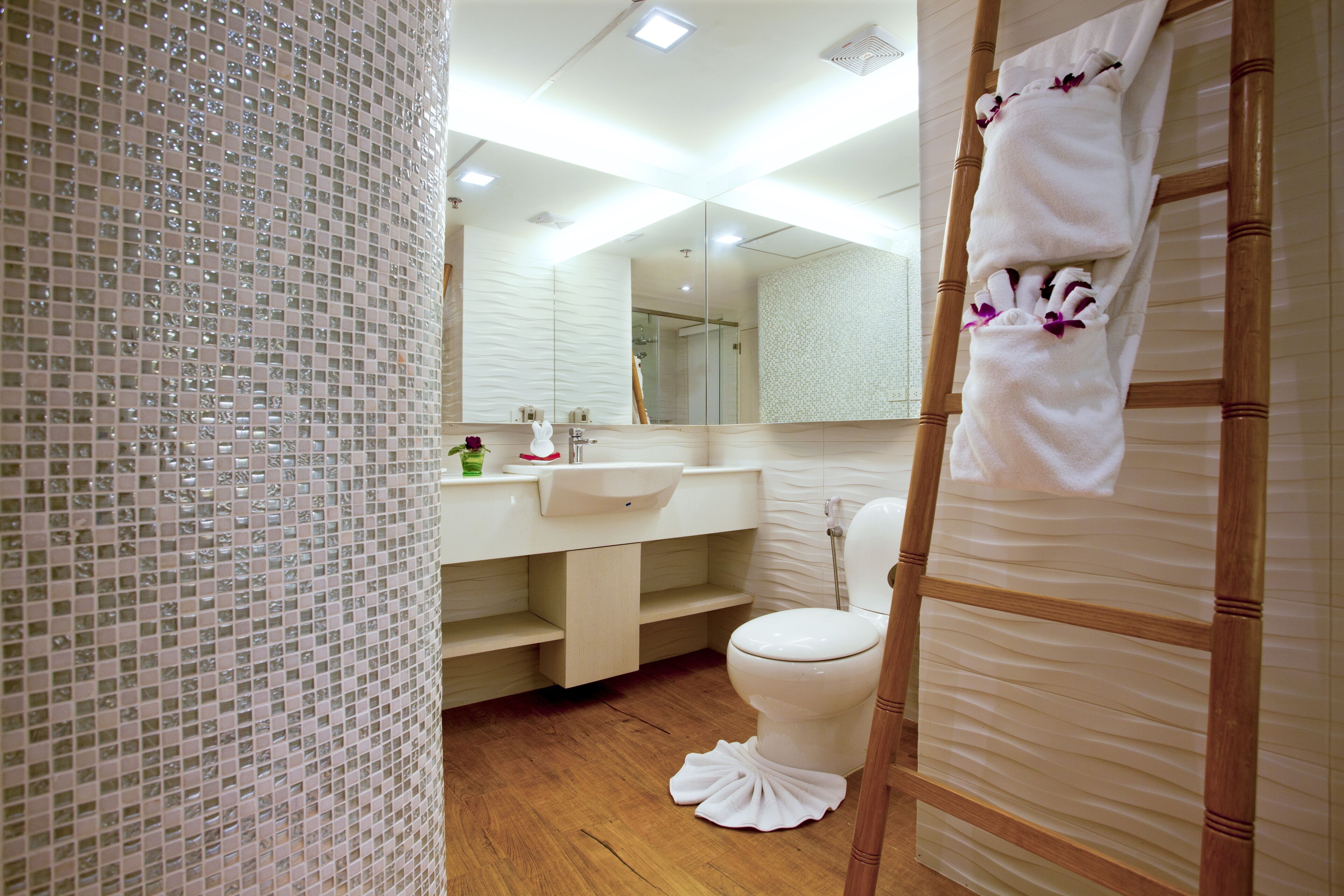 Une salle de bain moderne avec un plancher en bois, des toilettes blanches, un lavabo et un miroir.