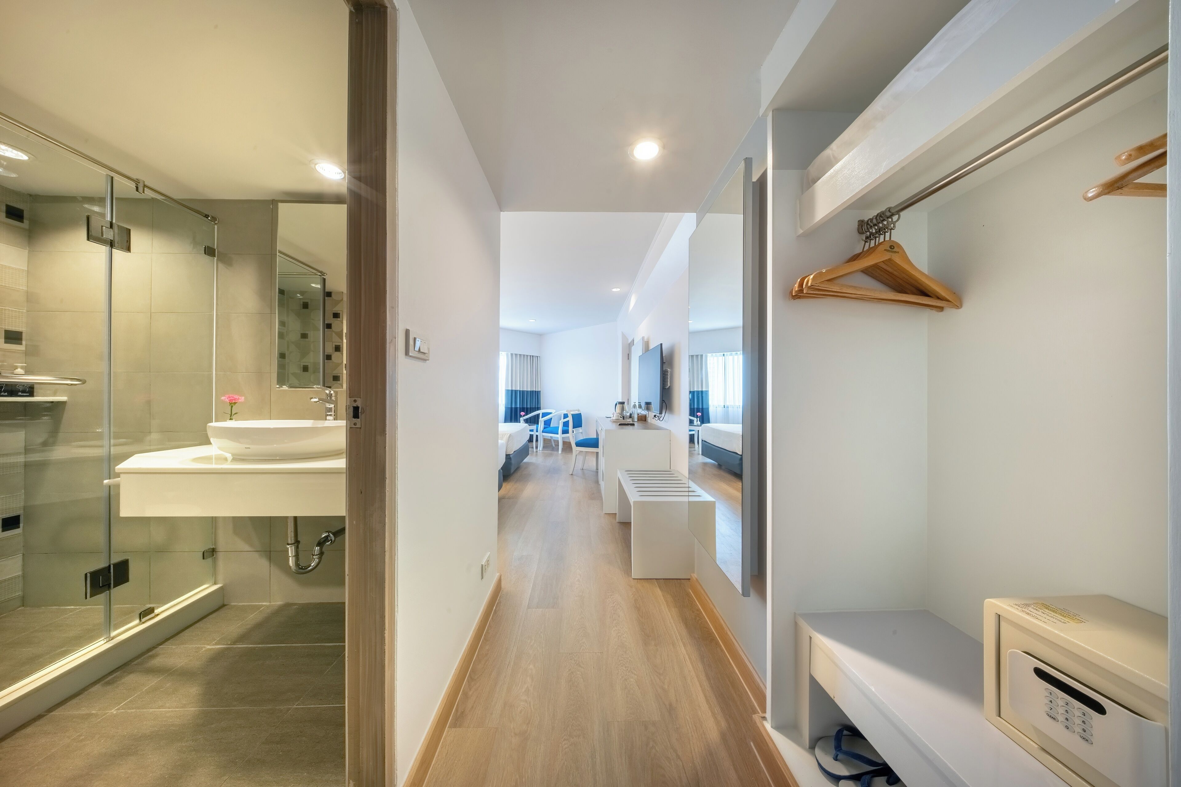 Un baño de hotel moderno con cabina de ducha de vidrio, un lavamanos blanco y suelo de madera.