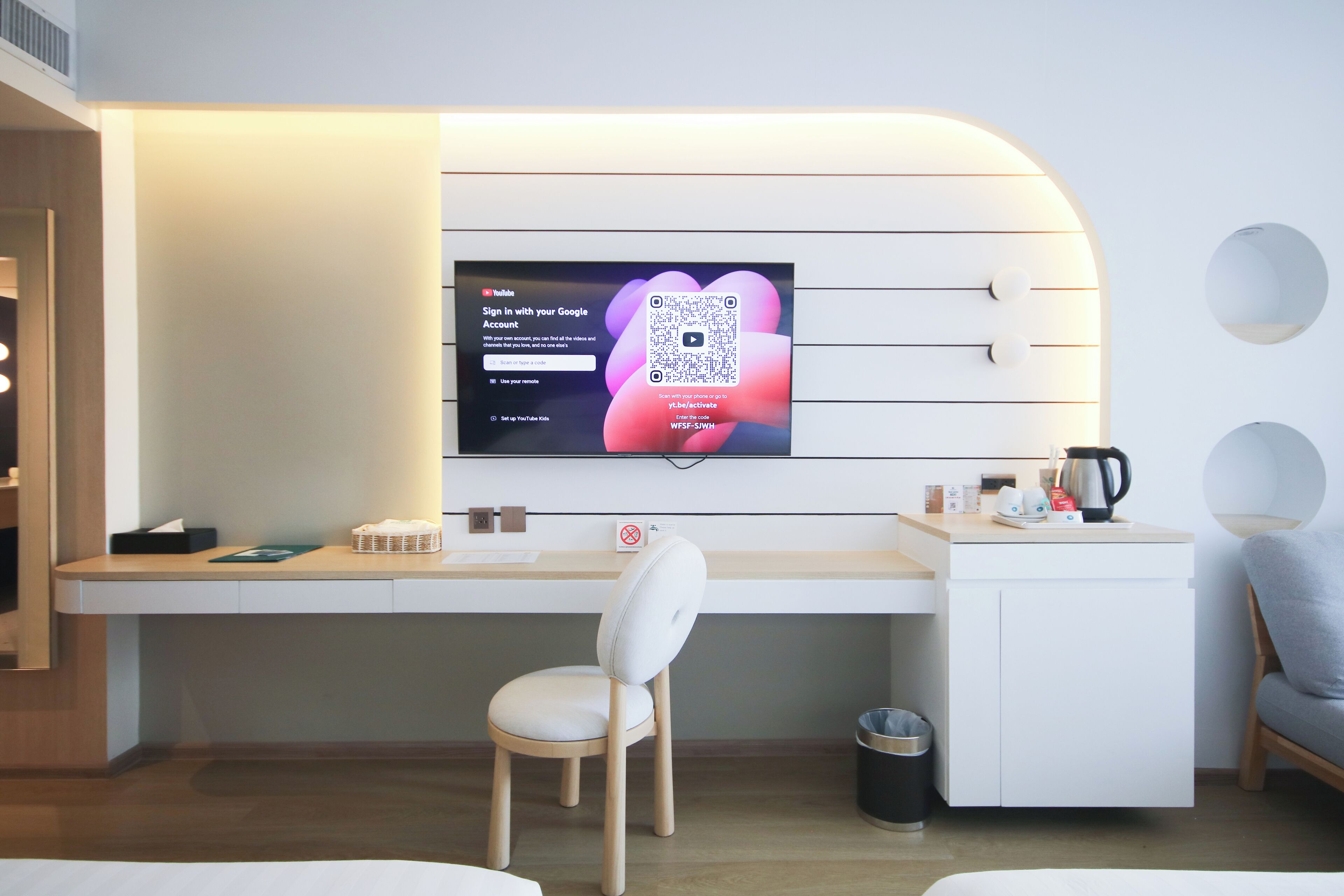 A modern hotel room with a desk, a chair, a television, and a bed.