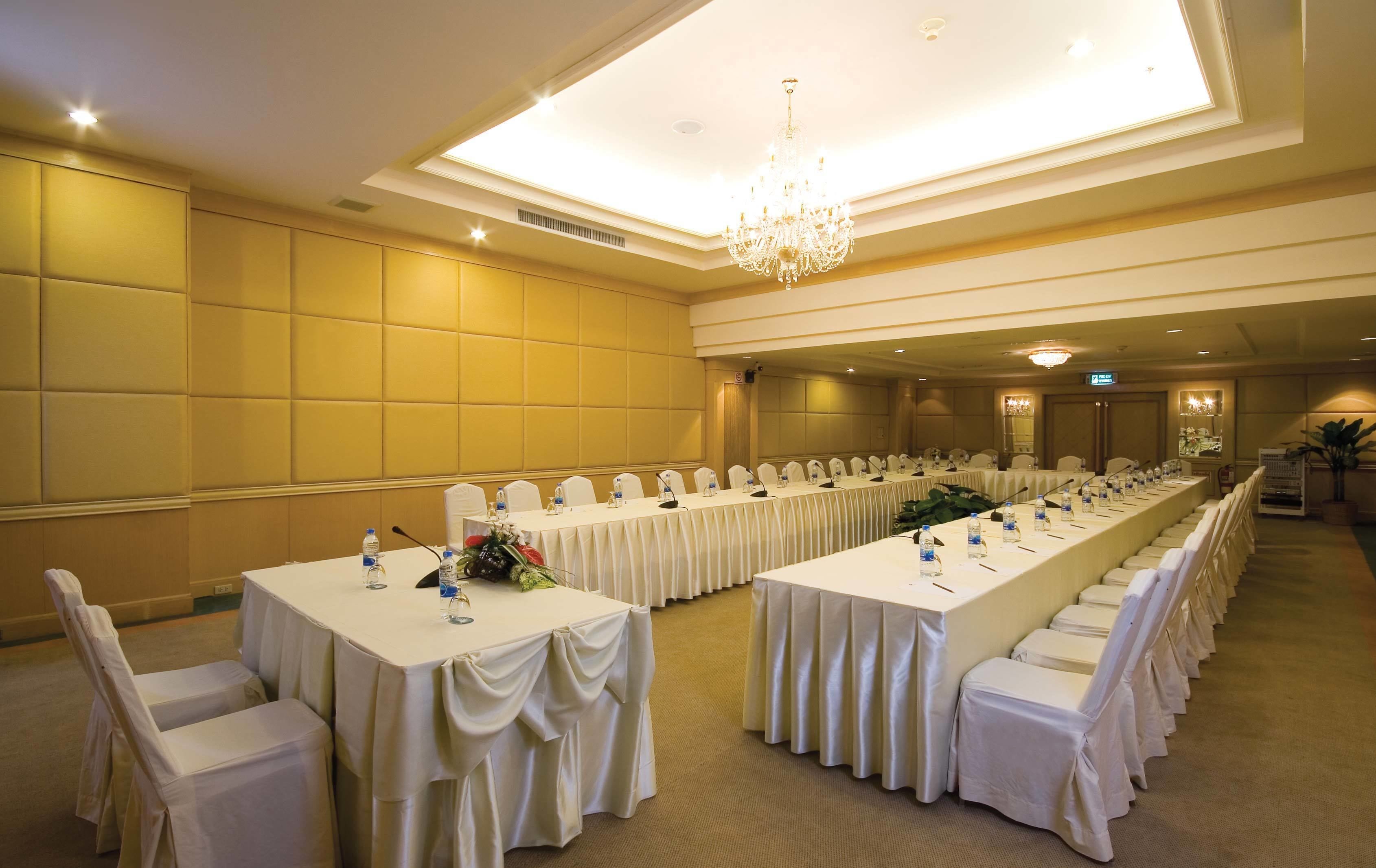 Une salle de conférence avec de longues tables, des chaises blanches et un lustre.