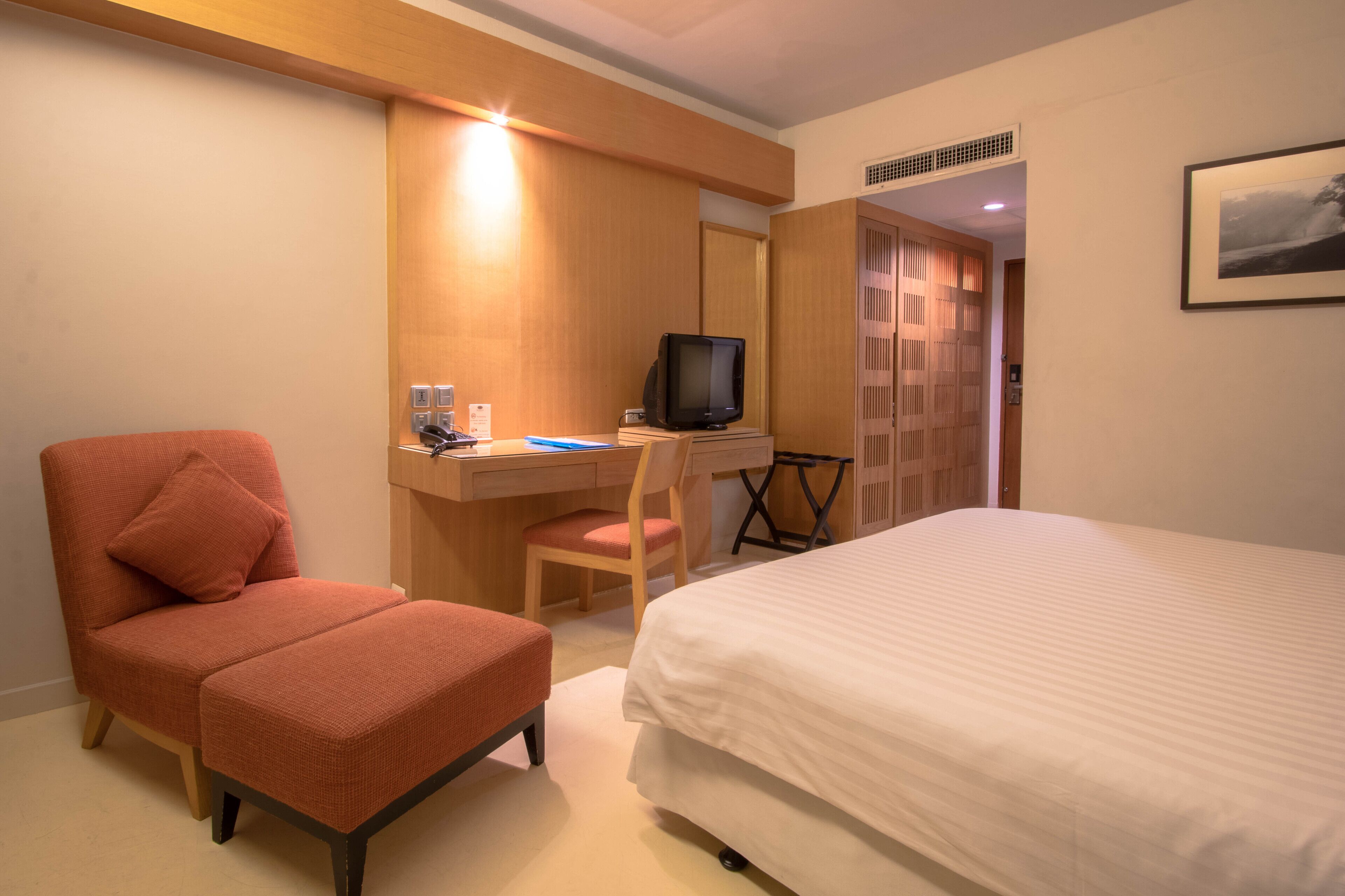 Una habitación de hotel con una cama, un escritorio con computadora, una silla y un televisor.