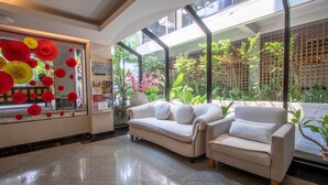 A modern lobby with two sofas, a glass wall with red paper decorations, and a view of greenery outside. - The Residence Rajtaevee Hotel (Bangkok)
