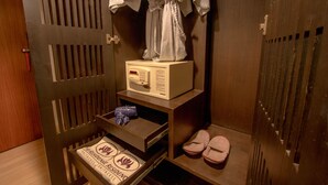 A hotel room with a wooden door, a robe hanging on the door, a microwave on a shelf, a pair of slippers, and a small table with a towel. - The Residence Rajtaevee Hotel (Bangkok)