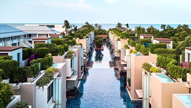 Un resort con piscina infinita central, edificios modernos y vista al mar.
