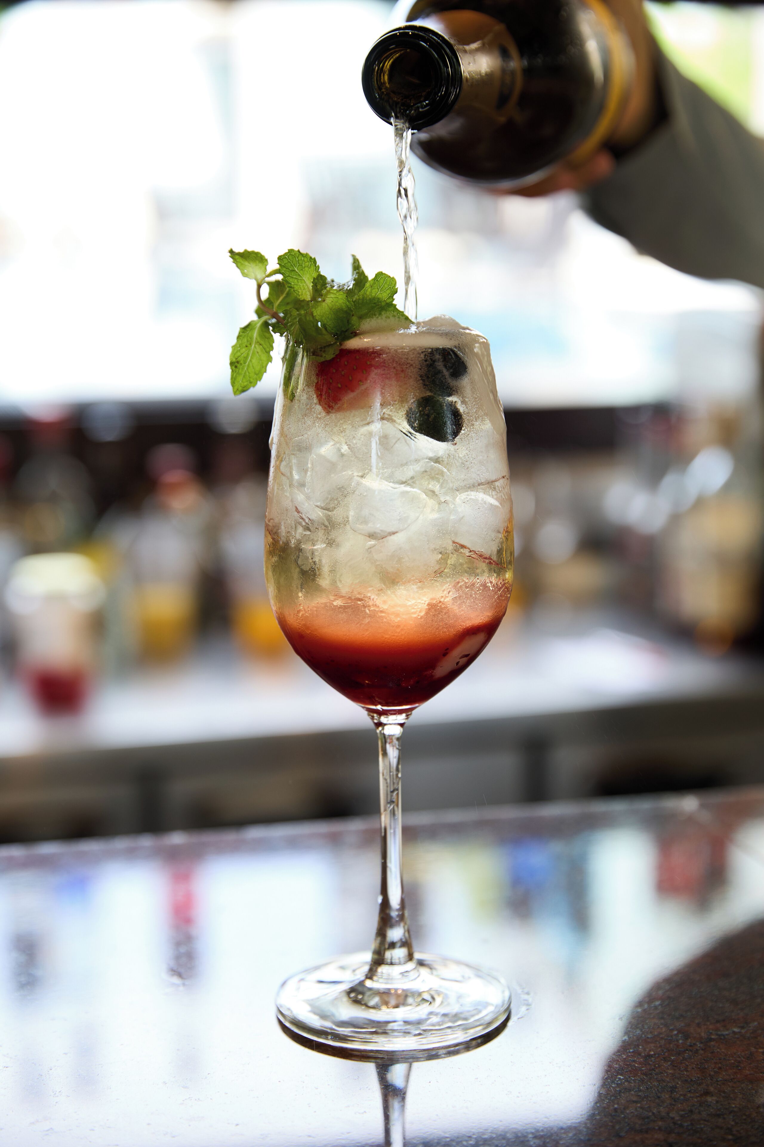 A cocktail being poured into a glass with ice and garnished with mint leaves.