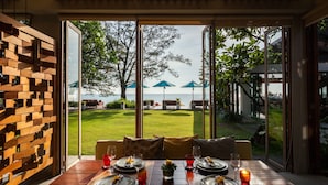 Un comedor con una mesa dispuesta para cuatro personas, ventanas amplias y vistas a un jardín con sombrillas.