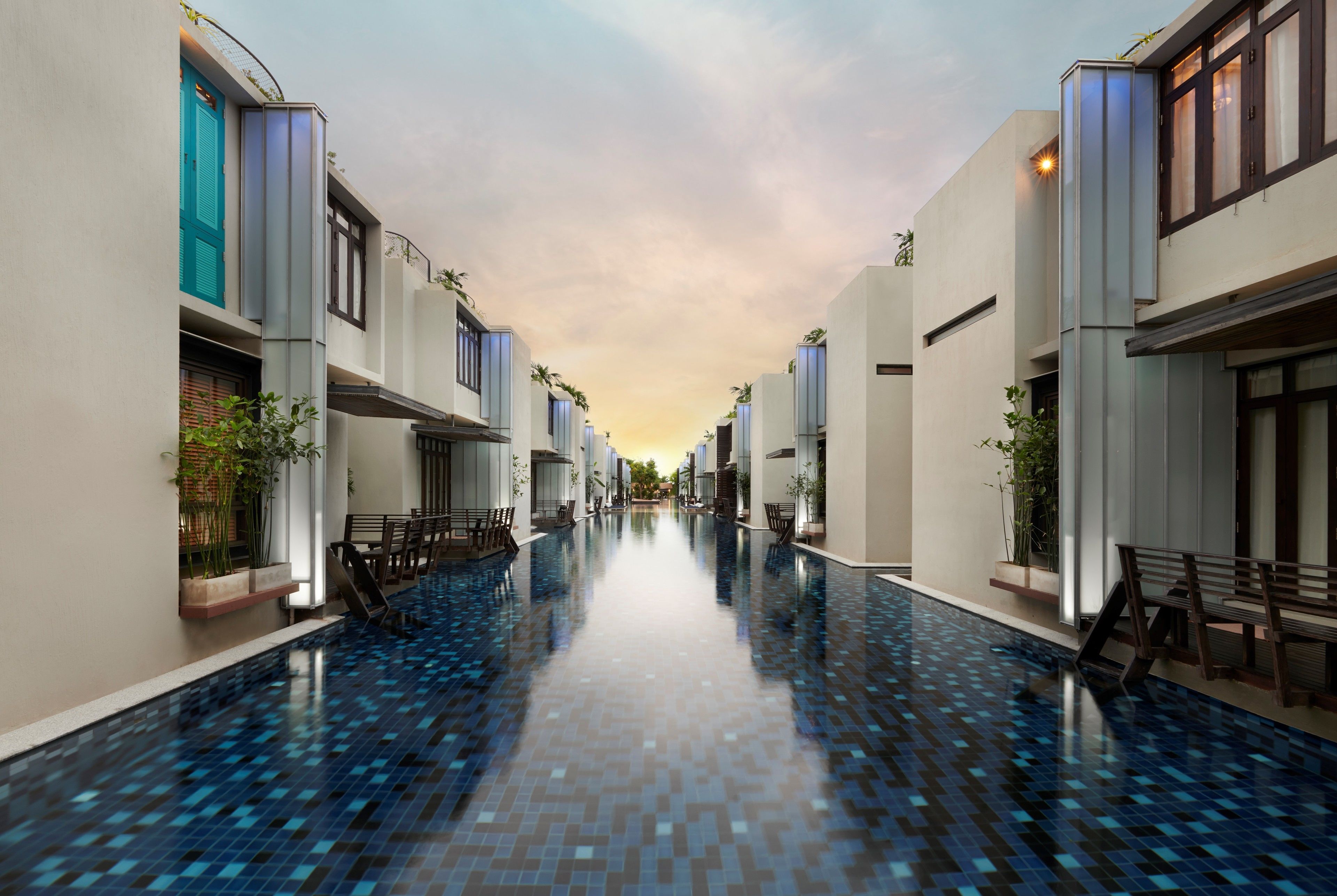 A modern hotel corridor with a central pool, featuring clean lines, balconies, and potted plants.