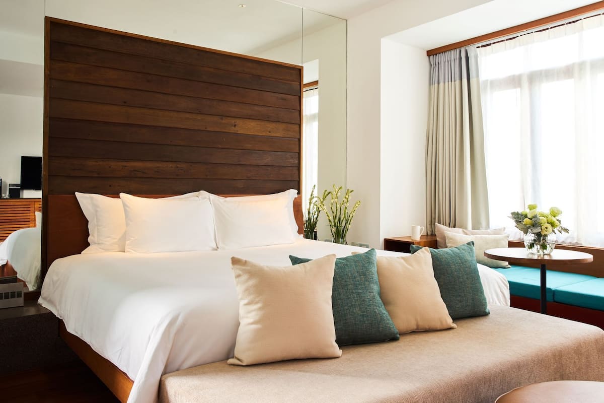 A hotel room with a large bed, a sofa, a small table with a vase of flowers, and a window with curtains.