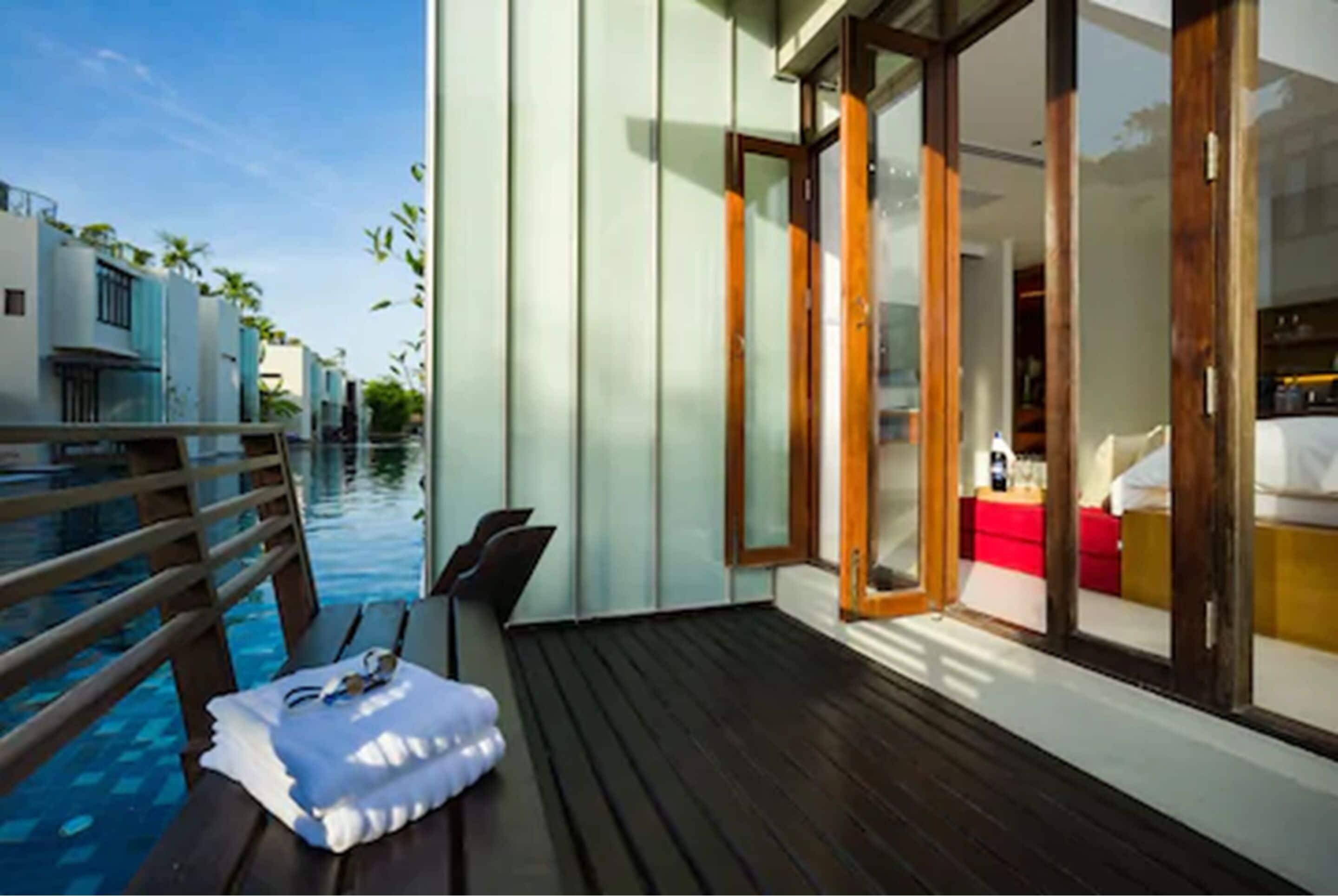 A modern poolside area with a wooden deck, a lounge chair, and a small table with a towel and sunglasses.