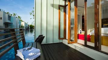A modern poolside area with a wooden deck, a lounge chair, and a small table with a towel and sunglasses.