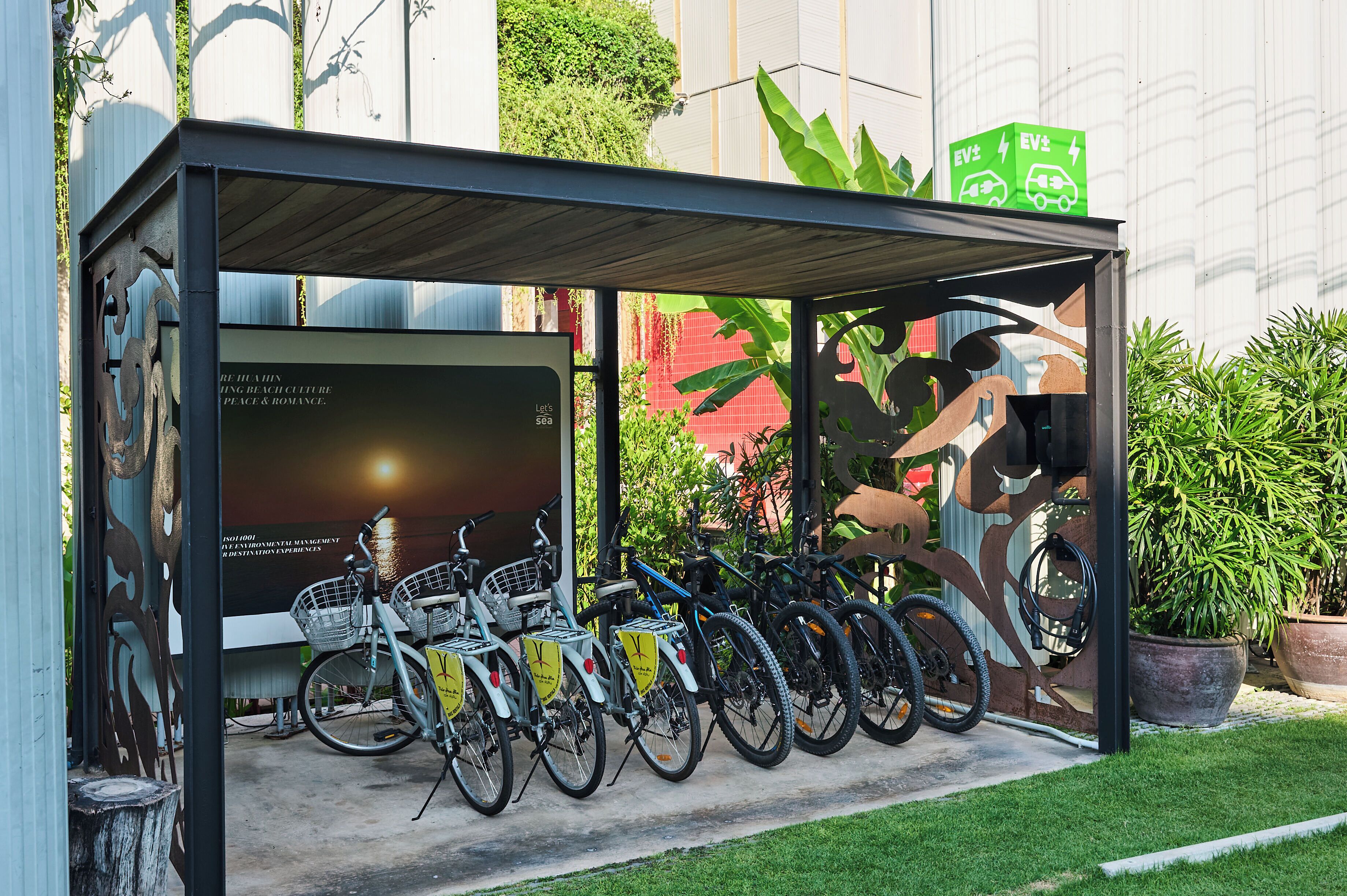 A covered bike parking area with bicycles, a mural, and a green EV charging box.