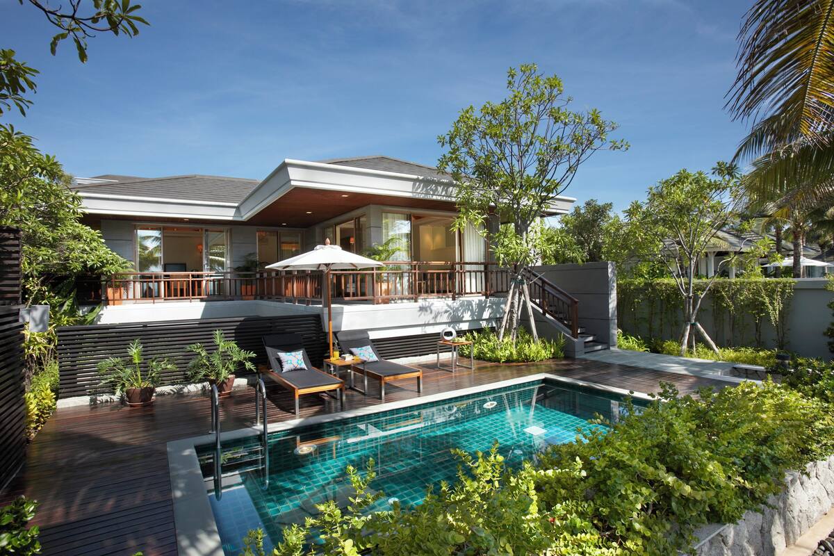 Una casa moderna con piscina, mobiliario exterior y abundante vegetación.
