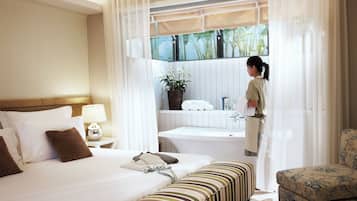 A hotel room with a bed, a sitting area, a bathtub, and a window with a view of greenery.