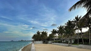 Ein Strand mit einer Betonpromenade, Palmen und einem Gebäude mit einem überdachten Bereich.