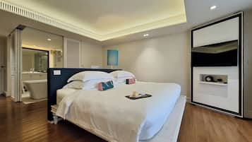 A modern hotel room with a large bed, a built-in desk, a vanity with a mirror, and a small shelf with toiletries.