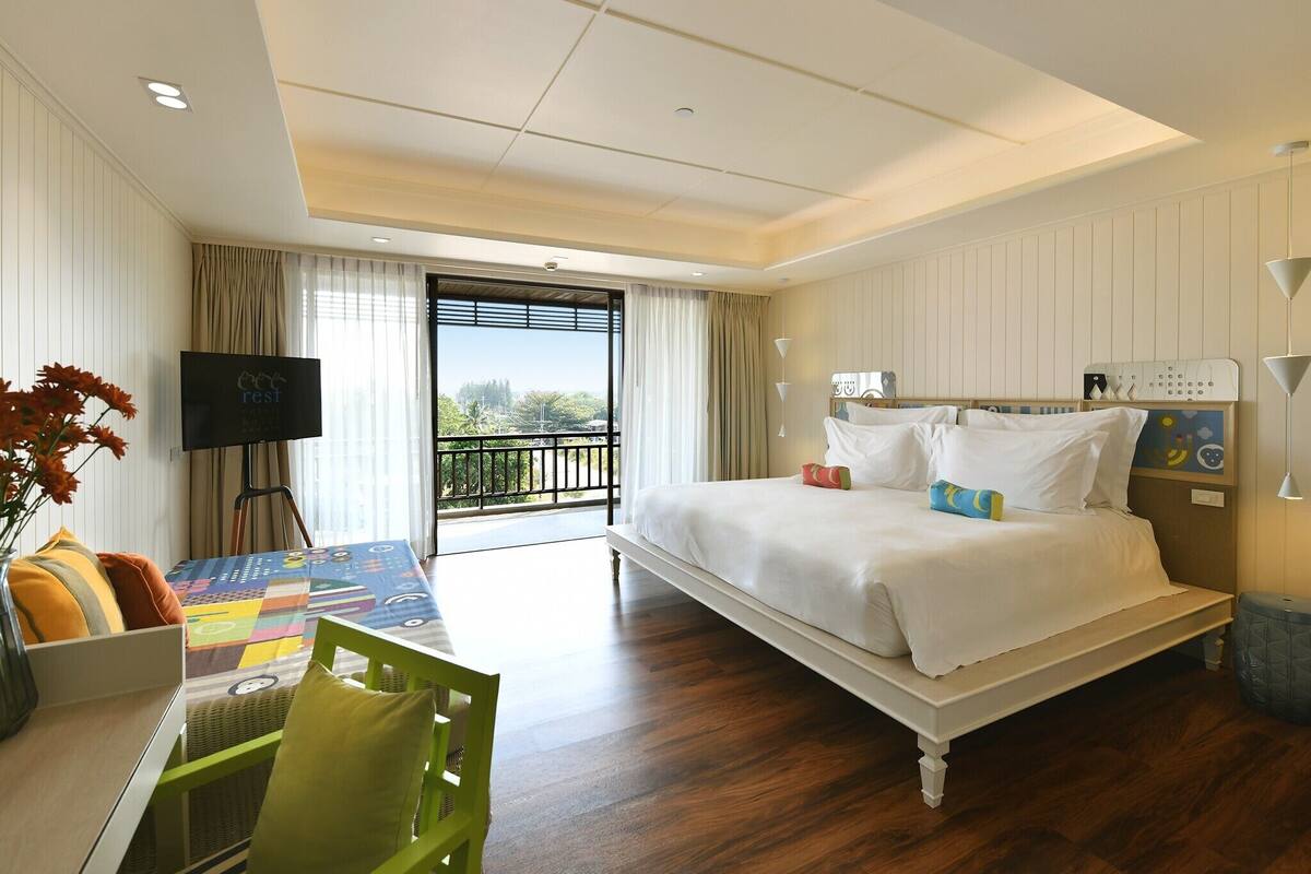 Habitación de hotel con cama, escritorio con silla, televisor y balcón con vistas.