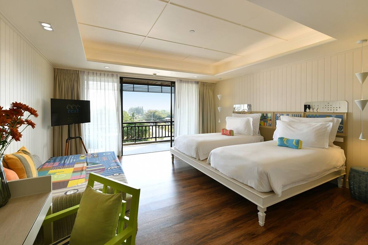 Habitación de hotel con dos camas, televisión, balcón y zona de comedor con mesa y sillas.