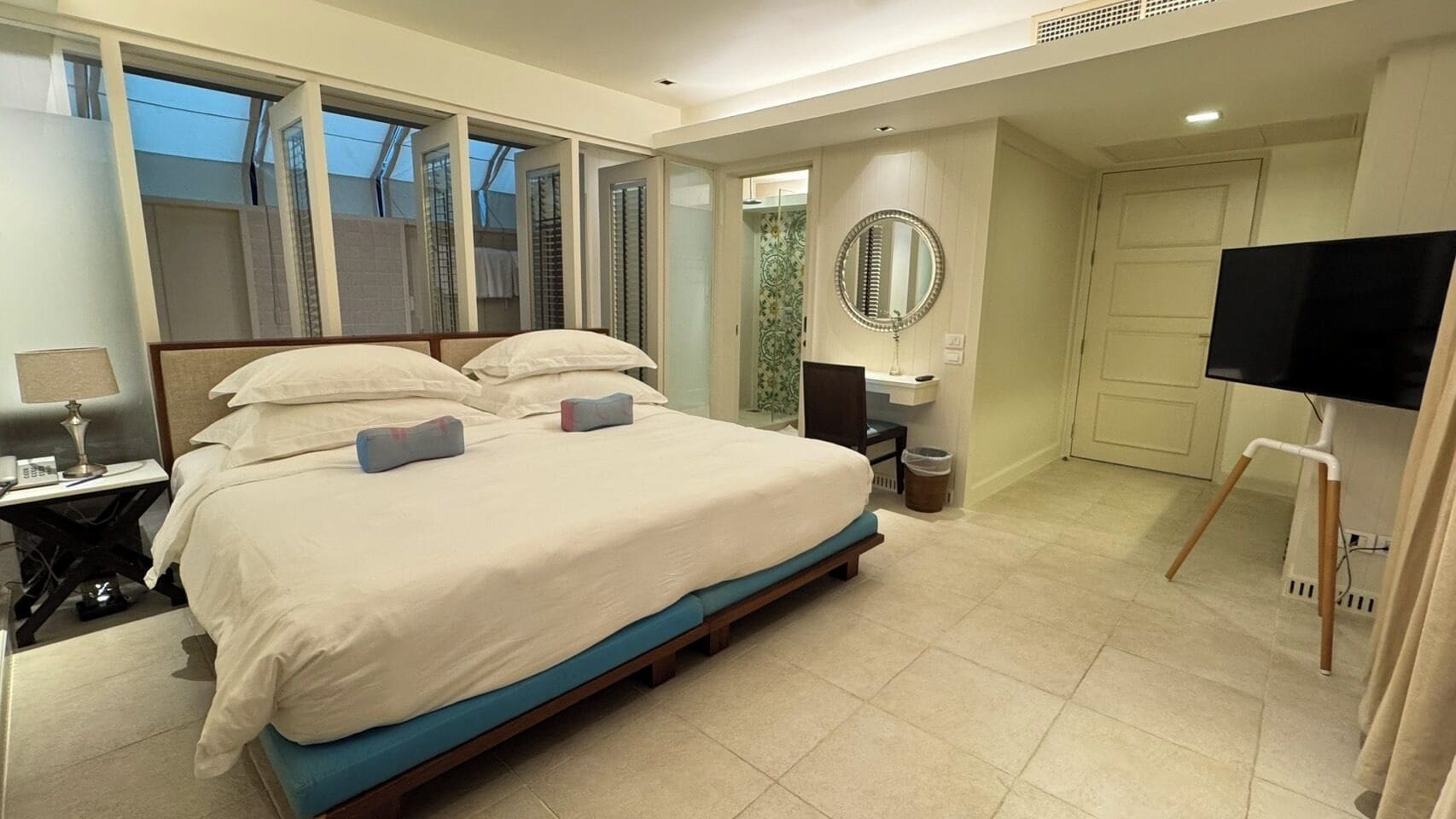 Habitación de hotel con una cama grande, un escritorio, una silla, un televisor y una ventana con persianas.